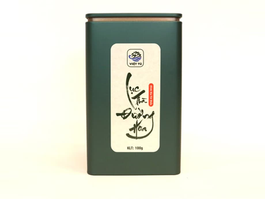 Hộp thiếc xanh đậm dán nhãn viết thư pháp, chụp trên nền trắng